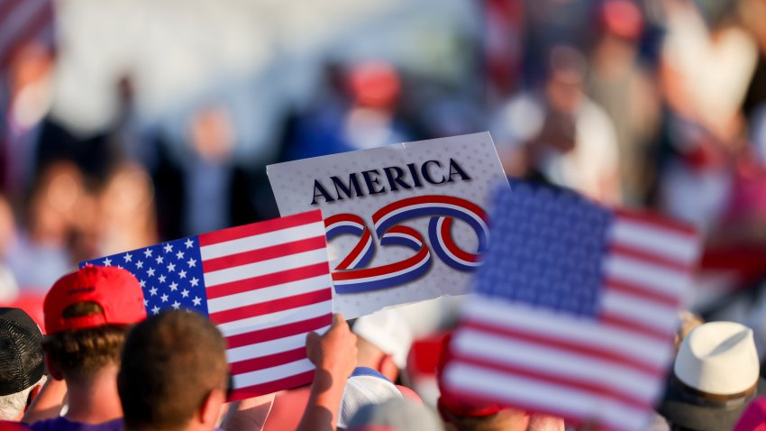Attendees hold US flags and an “America 250” sign during an event with US President Donald Trump, not pictured, at the Iowa State Fairgrounds in Des Moines, Iowa, US, on Thursday, July 3, 2025. Trump intends to lay out his plans to celebrate the nations 250th anniversary, in addition to emphasizing his bid to codify tax, immigration and welfare reforms in Congress. Photographer: Scott Morgan/Bloomberg via Getty Images
